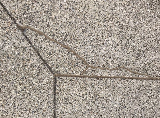 Aggregate concrete crack filled with concrete caulk and blended in to surrounding concrete