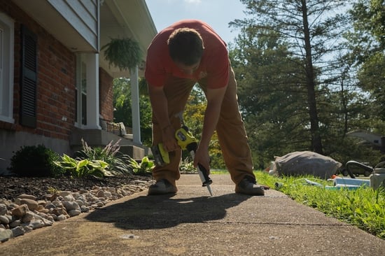 Man bending over to apply caulk to sidewalk crack with electric caulk gun