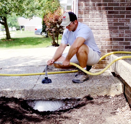 Man filling void under concrete slab with stone slurry grout leveling