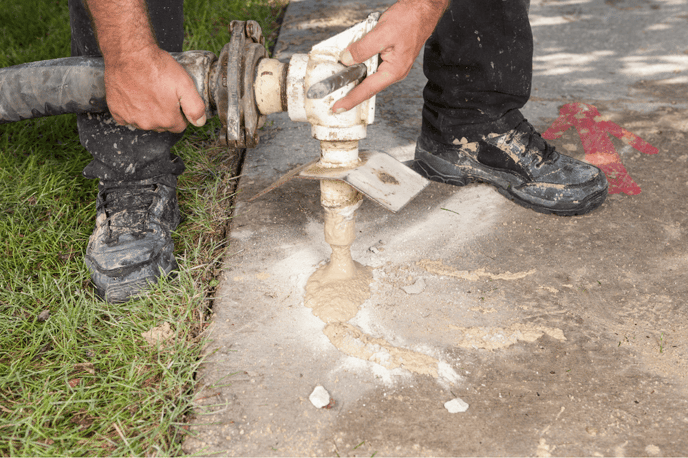 Mudjacking technician pumping mud material under sunken concrete