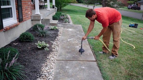 Man bending over to pump stone slurry grout under uneven sidewalk