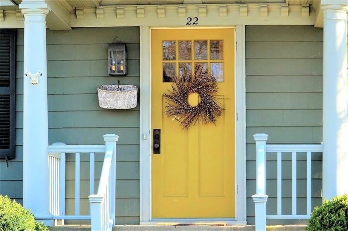 Yellow front door leading to front porch of house with green siding