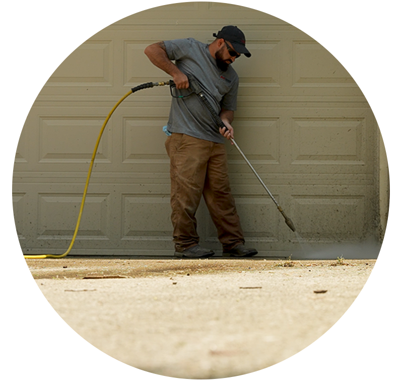 Man pressure washing driveway near garage door